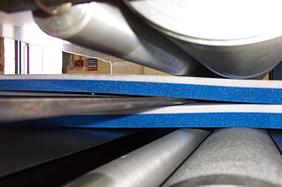 Driven rollers pulling foam sheets across blade